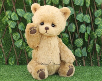 May include: A light brown teddy bear with a friendly expression, wearing a brown nose and brown paw pads. The bear is sitting on a green grassy surface and has its right paw raised in a waving gesture. The bear has the text "With love, Laisterinka" printed on its chest.