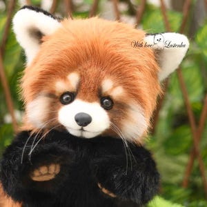 Puede incluir: Un peluche de panda rojo con un pelaje marr&oacute;n rojizo y esponjoso, patas negras y una nariz negra. El peluche tiene ojos grandes y expresivos y detalles blancos en las orejas y la cara. El texto "With love! Lastenka" es visible.