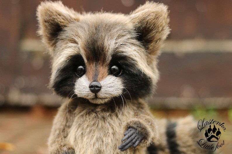 K&ouml;nnte beinhalten: Ein handgefertigtes Pl&uuml;sch-Waschb&auml;r mit detailliertem, realistischem Design. Der Waschb&auml;r hat ein braunes und graues Fell, schwarze Markierungen um die Augen und eine schwarze Nase. Das Pl&uuml;schtier hat einen freundlichen Ausdruck und ist ein Sammlerst&uuml;ck.