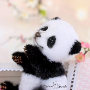 May include: A plush panda bear with black and white fur, brown paws, and a brown nose. The panda is looking upwards with its arms raised. The image has a soft, blurred background with pink flowers and the text "With love" and the name "Lastenka".