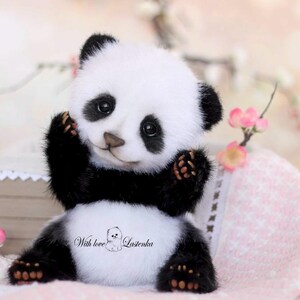 May include: A handmade panda bear plush toy with black and white fur, sitting with its arms raised. The panda has a sweet expression and is surrounded by pink flowers and a soft pink blanket. The text "With love" is visible on the panda's belly.