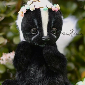 May include: A black and white skunk plush toy wearing a flower crown. The toy has a white stripe down its back and a cute, innocent expression. The toy is sitting on a bed of green leaves.