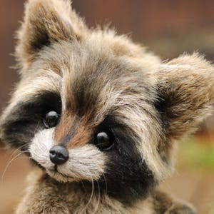 K&ouml;nnte beinhalten: Ein Pl&uuml;sch-Waschb&auml;r mit detailliertem, realistischem Design. Der Waschb&auml;r hat eine schwarze Nase, dunkle Augen und eine Mischung aus braunem und grauem Fell. Das Bild enth&auml;lt den Text "Lastenka Little foot" mit einem Pfotenabdruck.