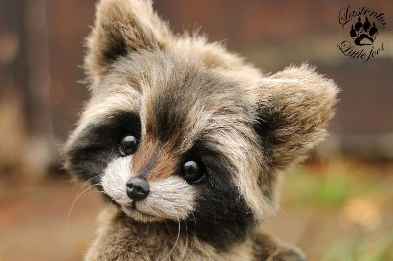 K&ouml;nnte beinhalten: Ein Pl&uuml;sch-Waschb&auml;r mit detailliertem, realistischem Design. Der Waschb&auml;r hat eine schwarze Nase, dunkle Augen und eine Mischung aus braunem und grauem Fell. Das Bild enth&auml;lt den Text "Lastenka Little foot" mit einem Pfotenabdruck.