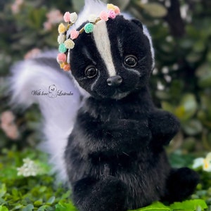May include: A black and white skunk plush toy wearing a colorful flower crown. The skunk is sitting on a bed of green leaves. "With love, Losenka" is written on the plush toy.
