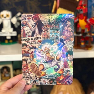 May include: A rectangular metal print featuring a vibrant collage of One Piece manga panels and illustrations. The artwork showcases Monkey D. Luffy in various forms, including his Gear 5 transformation, alongside text reading Monkey D. Luffy and King of the Pirates.