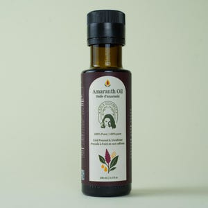 Può includere: Una bottiglia di vetro marrone scuro di Olio di Amaranto con tappo nero. L'etichetta recita "Amaranth Oil" e "Huile d'amarante". La bottiglia contiene 100 ml di olio spremuto a freddo e non raffinato.