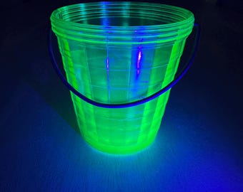 May include: A neon green bucket with a black handle. The bucket has a grid pattern and is illuminated with a bright green glow. The background is dark with blue lighting.