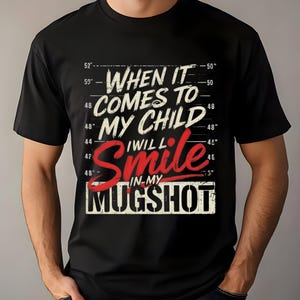 May include: Black t-shirt with the text "WHEN IT COMES TO MY CHILD I WILL SMILE IN MY MUGSHOT" in white and red lettering. The shirt has a mugshot-style design with height measurements.
