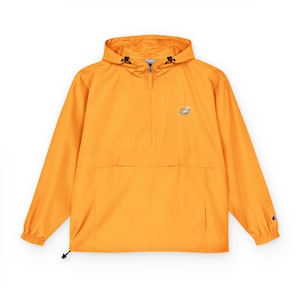 May include: A bright orange anorak jacket with a hood and a half-zip closure. The jacket features a kangaroo pocket and a small logo on the chest. The sleeves have elastic cuffs, and the jacket has a drawstring at the hem. A Champion logo is visible on the sleeve.
