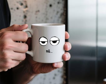 May include: A white ceramic mug featuring a graphic of two tired, half-closed eyes and the text "nö..." printed in black. The mug has a smooth, glossy finish and a curved handle on the side, designed for holding hot or cold beverages.