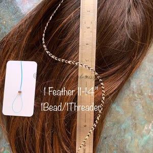 picture of one single grizzly feather laying against a 12inch silver ruler and on top of a brown wig