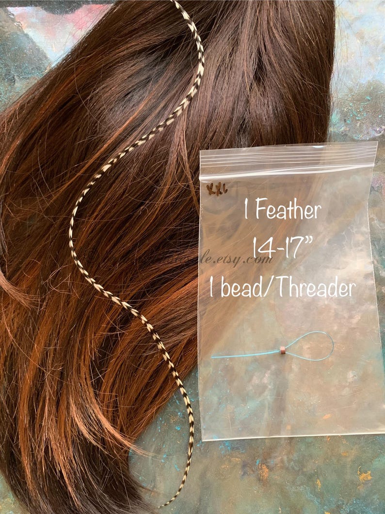 1 XXL hair feather shown against brown hair with 1 silicone bead and floss threader in a clear polybag