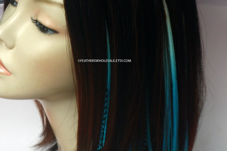 Puede incluir: Una modelo con el pelo largo y casta&ntilde;o con extensiones de pelo de plumas azules y blancas. El texto "@FEATHERSWHOLESALE.ETSY.COM" es visible en la imagen.