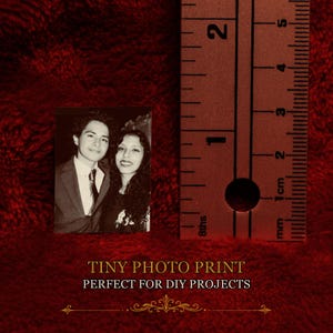 May include: A small rectangular black and white photograph featuring a person in a suit and tie next to a person with long dark hair. A metal ruler is positioned to the right, showing the print height is approximately 2.25 inches tall.
