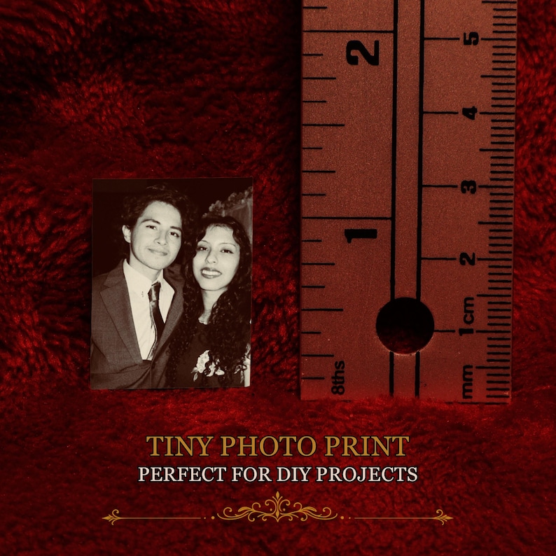May include: A small rectangular black and white photograph featuring a person in a suit and tie next to a person with long dark hair. A metal ruler is positioned to the right, showing the print height is approximately 2.25 inches tall.