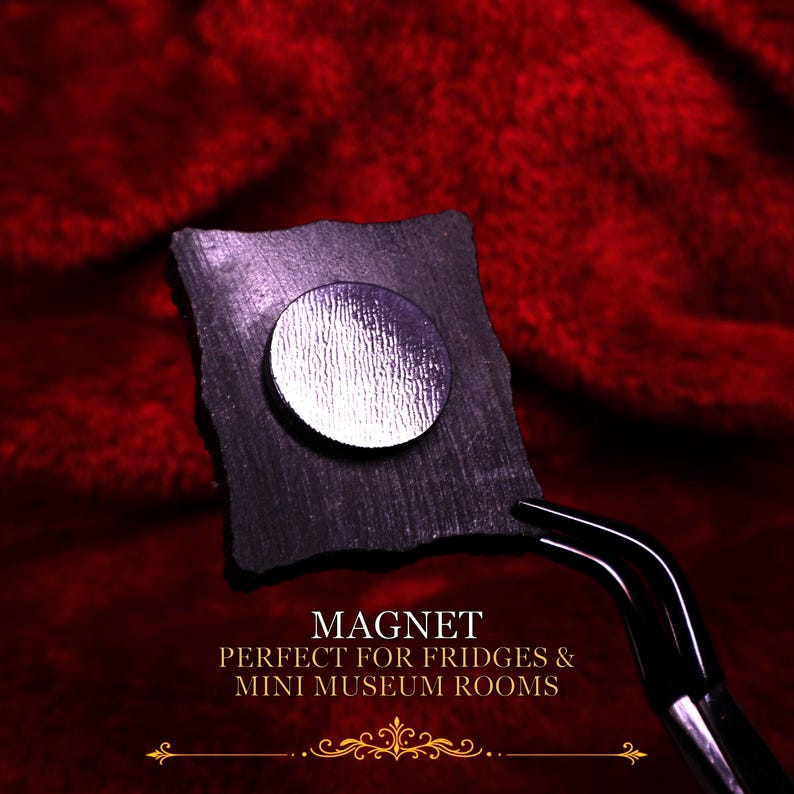 May include: A square black magnet with a circular silver metallic center, held by a pair of black tweezers. The text on the image reads: MAGNET, PERFECT FOR FRIDGES & MINI MUSEUM ROOMS, accompanied by a decorative gold horizontal line graphic.