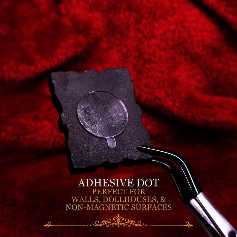 May include: A small black rectangular piece with a clear circular adhesive dot attached to the center. The object is held by a pair of black metal tweezers. The text on the image reads: ADHESIVE DOT PERFECT FOR WALLS, DOLLHOUSES, & NON-MAGNETIC SURFACES.