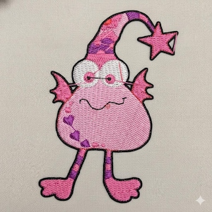 May include: Embroidered pink monster with a whimsical design. Features a patterned hat, star, and heart accents. The monster has large white eyes, small wings, and striped legs, all outlined in black.
