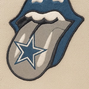 Puede incluir: Parche bordado con el icónico logo de la lengua de los Rolling Stones, con un diseño de estrella azul y blanca en la lengua. Los labios son azules con reflejos blancos, contorneados en negro, sobre un fondo beige.