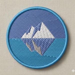 May include: Circular embroidered patch with a mountain and water design. The patch has a blue border and features a mountain range reflected in water, using shades of blue, white, and grey. Suitable for clothing or accessories.