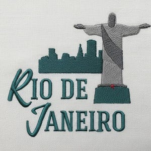 May include: Embroidered design with the words "Rio de Janeiro" in teal script, a teal skyline, and a grey statue of Christ the Redeemer. The design is set against a white background.