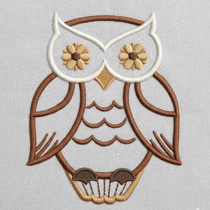 May include: Embroidered owl design in brown, tan, and white. The owl features flower-shaped eyes and a detailed outline. The design is on a light gray fabric, showcasing the intricate stitching and color contrast. A decorative element suitable for various craft projects.
