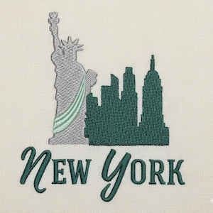 May include: Embroidered design featuring the Statue of Liberty and a cityscape in shades of gray and green. The word "New York" is written in a cursive font below the illustration. The design is on a cream-colored fabric.