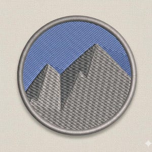 May include: Embroidered patch with a mountain range design. The circular patch has a grey border. The mountains are grey with a textured appearance, set against a blue sky background.