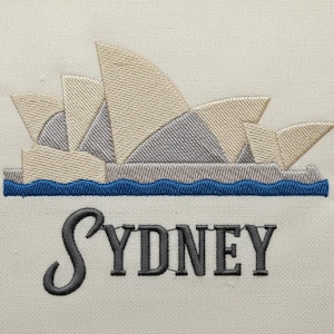 Op de afbeelding: Geborduurd ontwerp met het Sydney Opera House in beige, grijs en blauw. Het iconische gebouw staat boven een blauwe golflijn, met de stadsnaam "SYDNEY" eronder geborduurd in grijs.