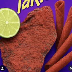 Peut inclure: Gros plan d'une tranche de citron vert et de collations rouges sur fond violet. Les collations comprennent un grand morceau texturé et plusieurs morceaux roulés. Le mot "Takis" est visible en jaune en haut.