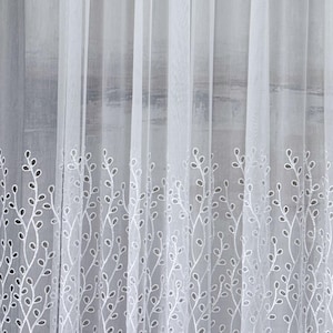 Puede incluir: Un panel de cortina blanco transparente con un patrón bordado vertical de tallos delicados y repetitivos en forma de enredadera con pequeñas hojas ovaladas. El bordado es blanco y crea un diseño botánico texturizado en la parte inferior.
