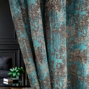May include: Close-up of textured teal and grey patterned curtains. The fabric has a woven appearance with a mottled design, featuring splashes of teal against a backdrop of grey and brown tones. The curtains are draped, showing folds and texture.