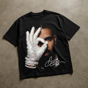Puede incluir: Una camiseta negra de manga corta con un estampado gráfico de una persona con barba, parcialmente oculta por una mano con un guante blanco de lentejuelas. El guante hace un gesto de OK. Se aprecian una firma blanca y una pulsera con el texto ICEMAN.