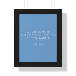 May include: Framed wall art with a black frame. The artwork features a light blue background with white text that reads "WE SUFFER MORE OFTEN IN IMAGINATION THAN IN REALITY -SENECA."