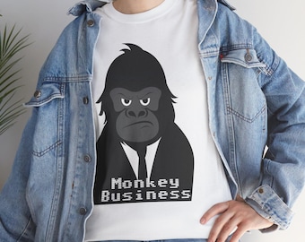 May include: White t-shirt featuring a black and gray illustration of a gorilla in a suit and tie. The text "Monkey Business" is printed below the gorilla. The shirt is worn with a denim jacket.