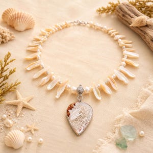 May include: A handcrafted necklace featuring a pearlescent, cream-colored design. The necklace has a central pendant with a unique, organic pattern, and is accented with pearls and shell-shaped elements. The necklace is set against a neutral background with seashells.