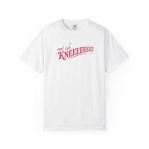 May include: A white short-sleeved t-shirt featuring the red text "mel luh KNEEEEEEEE" printed across the chest. The design includes small red heart and star accents surrounding the lettering, which is set in a stylized, slightly arched font.