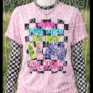 May include: Pink t-shirt with a checkerboard design and the text "Wanna Make a Pop and Drink Trail Sodas?". The shirt features a graphic of soda cans and a blue vehicle. The sleeves are black and white checkered.
