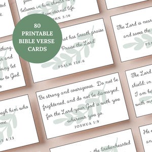 Op de afbeelding: Een verzameling van 80 afdrukbare Bijbelverskaarten. Elke kaart bevat een ander vers in elegant schrift, vergezeld van een delicaat groen bladerontwerp. De kaarten zijn gerangschikt op een lichtgekleurd oppervlak.
