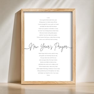May include: A framed print with a light wood-colored frame. The print features a poem titled "New Year's Prayer" in elegant script. The poem is printed in black on a white background, with the text arranged in a vertical format.