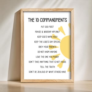 May include: A framed print with the text "THE 10 COMMANDMENTS" in black. The commandments are listed below the title. A yellow sun graphic is on the right side of the print. The frame is made of light-colored wood.