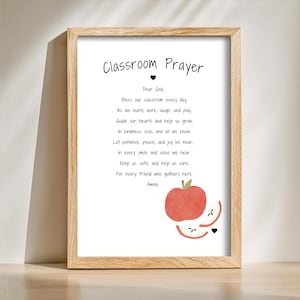 Pode incluir: Uma impressão emoldurada com o texto "Classroom Prayer" em escrita preta. A oração é impressa em preto sobre um fundo branco, com uma ilustração de maçã vermelha na parte inferior. A moldura é de madeira clara.