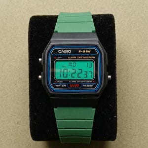 May include: A white ceramic mug with a black handle and the text "But First, Coffee" in a handwritten style. The mug is on a white surface. The mug is likely for hot beverages.