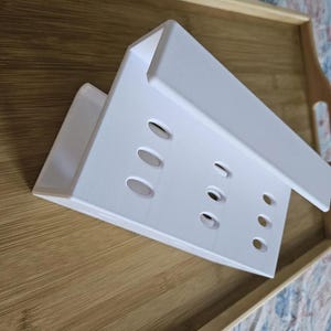 以下が含まれることがあります： 木製のトレイの上に置かれた、複数の楕円形の切り欠きのある白い長方形のオーガナイザー。 オーガナイザーは、一連の等間隔の穴を備えた垂直デザインです。 トレイは天然の木目を持っています。