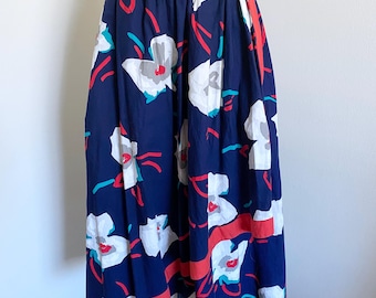 May include: A navy blue midi skirt with a white and red floral print. The skirt has a gathered waist and a straight hem.
