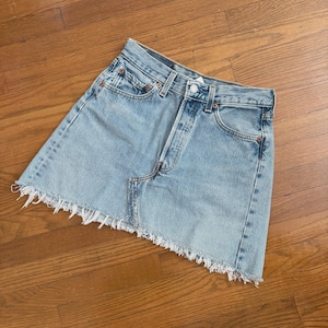 May include: Light blue denim skirt with a frayed hem. The skirt has a button and zipper closure, classic five-pocket design, and copper rivets. A casual, everyday wear item.