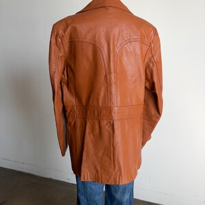 May include: A vintage brown leather jacket with a notched collar and tailored fit. The jacket features detailed stitching and a classic design. The jacket is displayed on a mannequin with blue jeans.