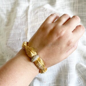 May include: A gold bracelet with a leaf design and a center piece of clear rhinestones.