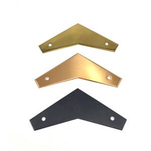 May include: Three metal arrow shapes in different finishes: gold, brass, and black. The arrows are all the same size and shape, with a pointed tip and two holes at the base.